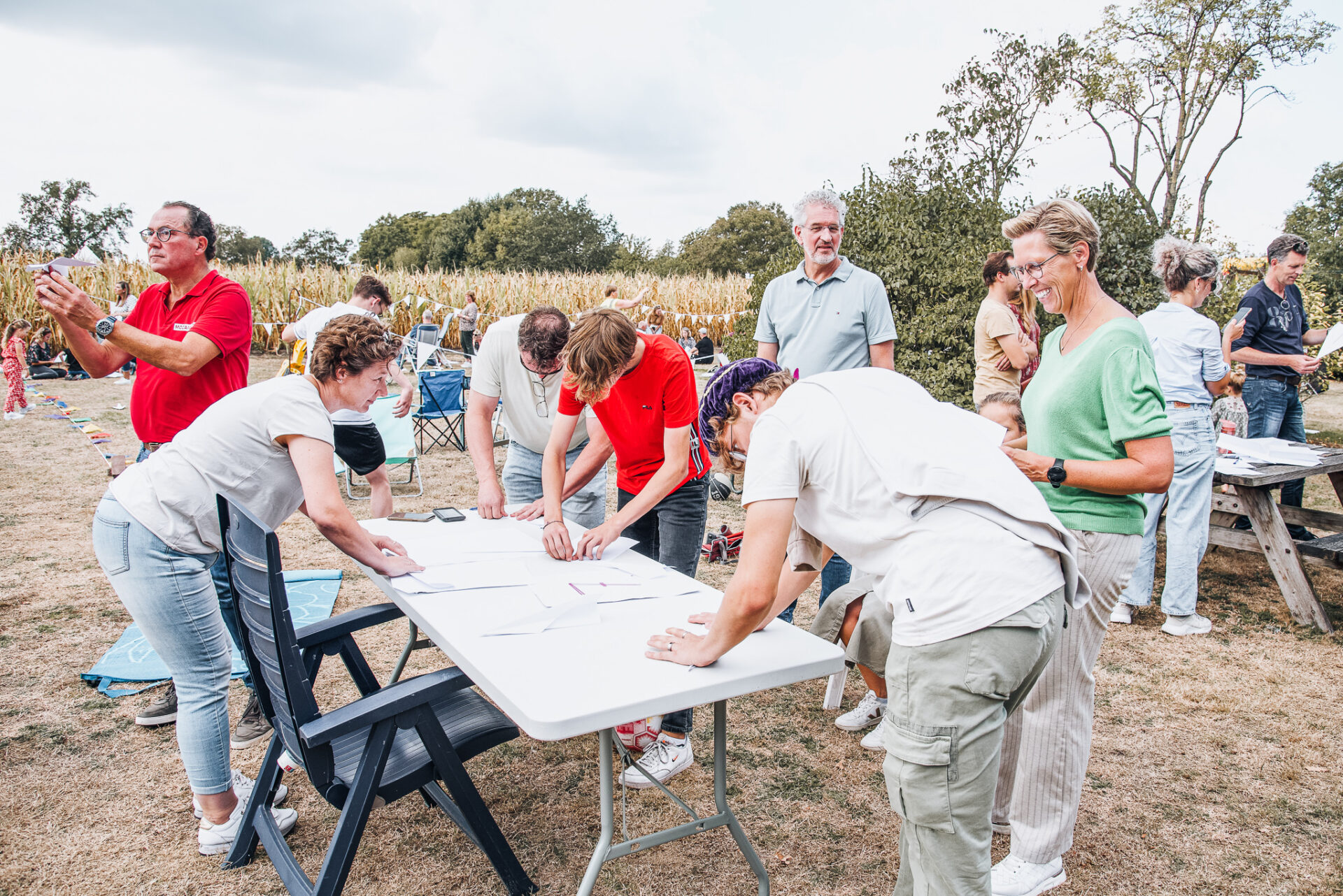 Bezoekers vouwen papieren vliegtuigjes rond een tafel op het veld