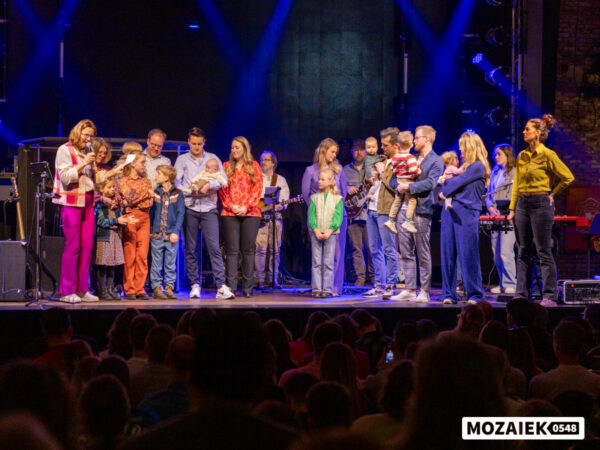 Gezinnen staan op het podium terwijl de volle zaal meekijkt tijdens een opdraagdienst van Mozaiek0548