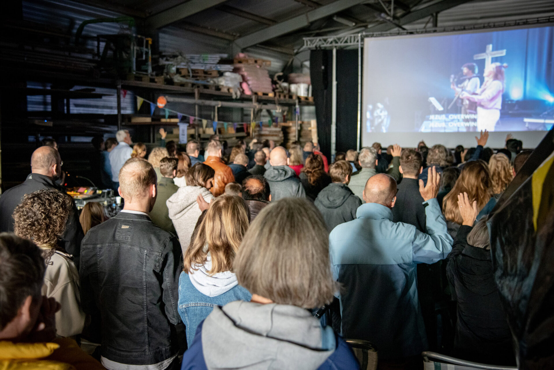 Bezoekers kijken naar de dienst op het grote scherm in de zaal