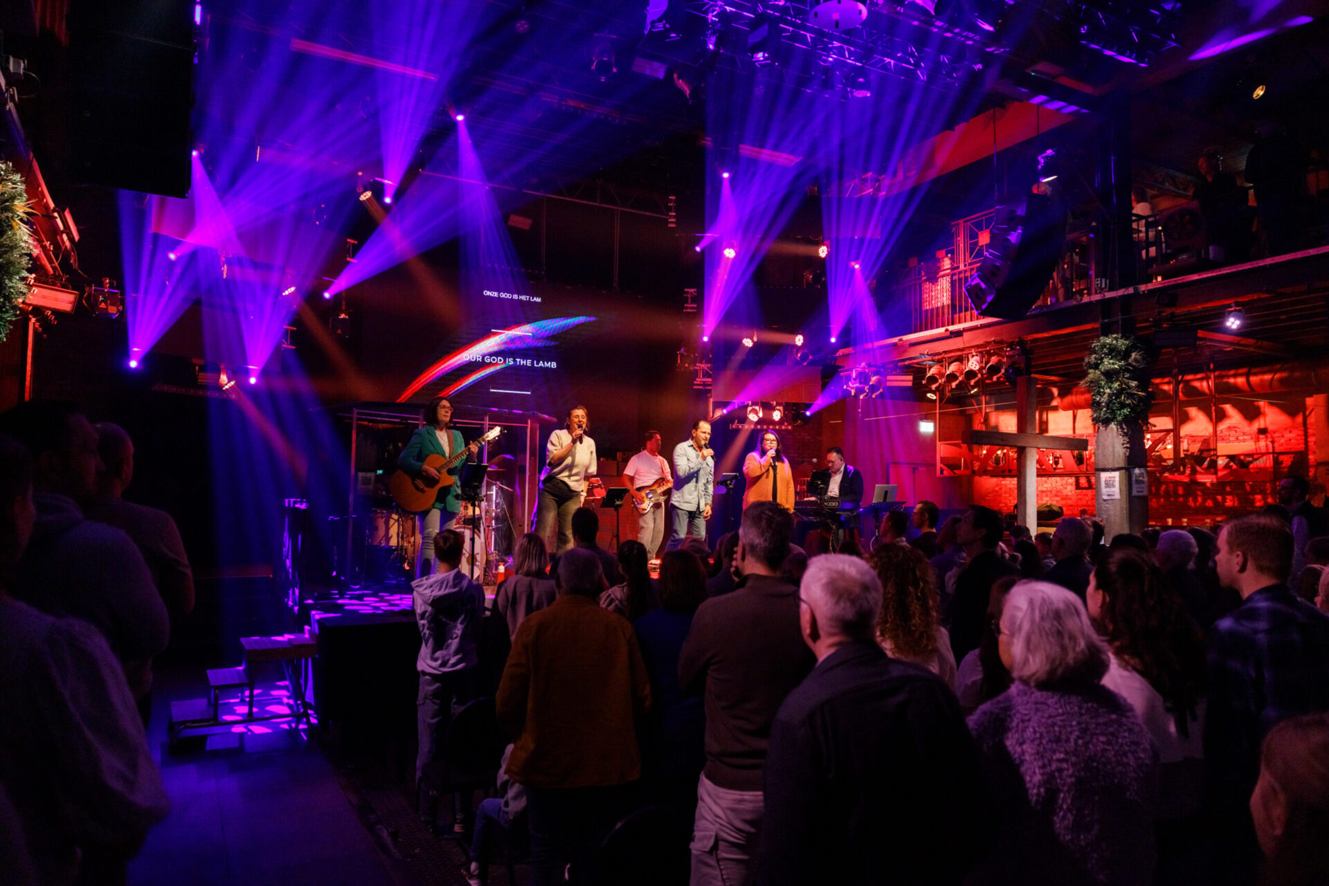 Bezoekers in de zaal met paars en rood licht tijdens de samenkomst