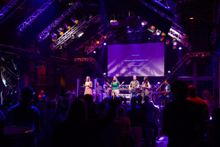 Zaal van Mozaiek0548 in paars licht met band op het podium en de tekst I worship you op het scherm