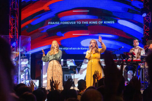 Twee zangeressen zingen tijdens de worship in Mozaiek0548 met opgeheven handen in de zaal
