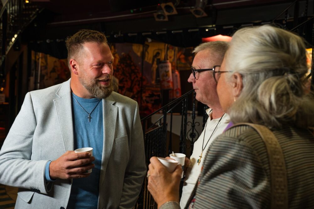 Gemeenteleden lachen samen tijdens een gesprek in de hal van Mozaiek0548